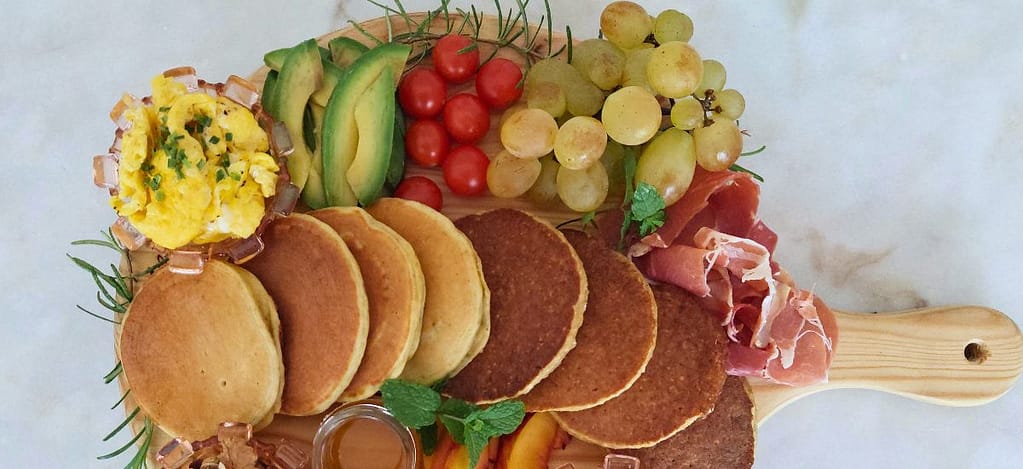 fruta, ovos mexidos e presunto , tomate cherry, frutos secos, e iogurte dispostos para um pequeno-almoço especial
