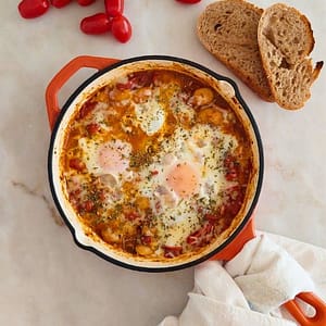 Molho de tomate com ovos escalfados e feijão branco, polvilhado com orégãos.