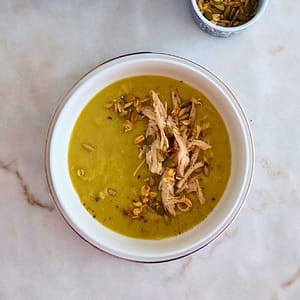 close - up de Sopa cremosa de brócolos com frango servida numa taça branca com topping de frango e granola