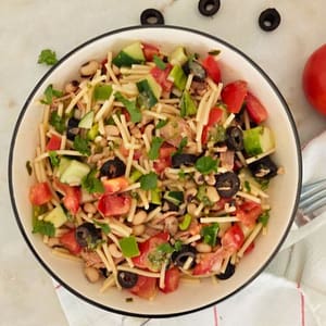 Salada de atum com massa e feijão frade vista de cima, servida num prato raso com guarnição de ervas