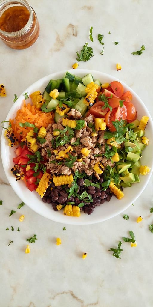 Salada de carne picada com feijão preto, milho e abacate, servida numa taça branca e com molho a acompanhar
