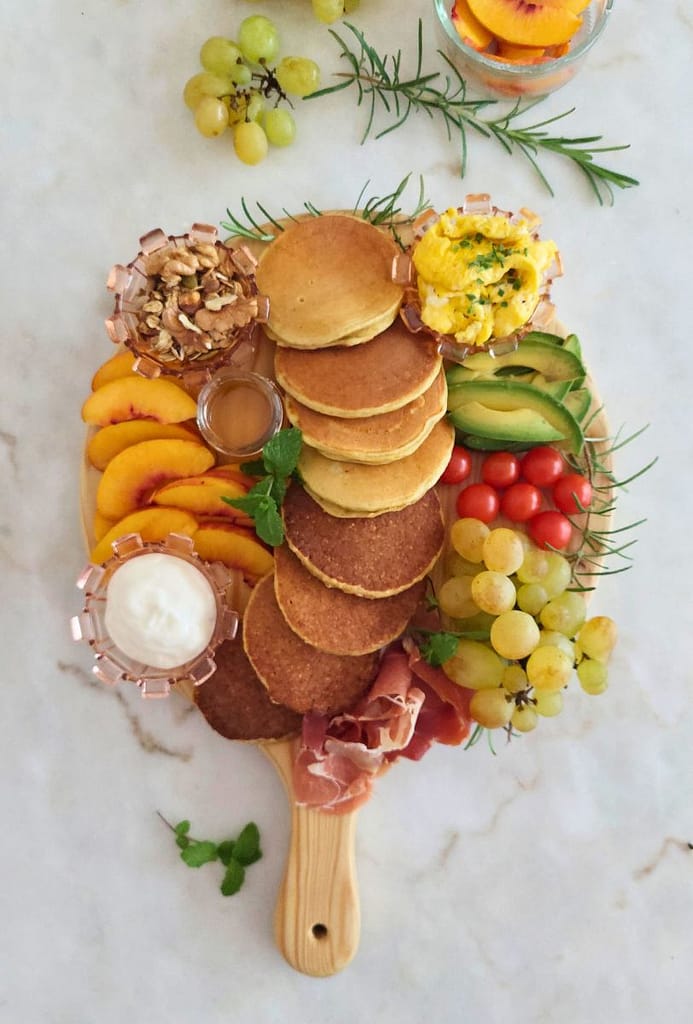 Tábua de panquecas para brunch montada com Panquecas, fruta, ovos mexidos e presunto, iogurte e mel