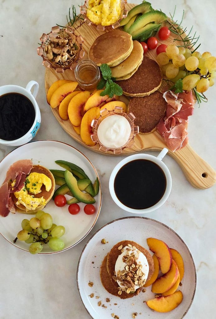 fruta, ovos mexidos e presunto , tomate cherry, frutos secos, e iogurte dispostos para um pequeno-almoço saudável