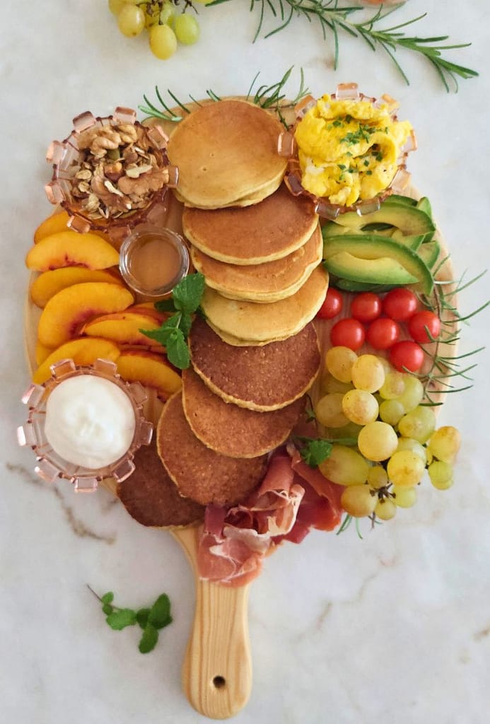 Panquecas, fruta, ovos mexidos e presunto, iogurte e mel disposto na Tábua de panquecas para brunch
