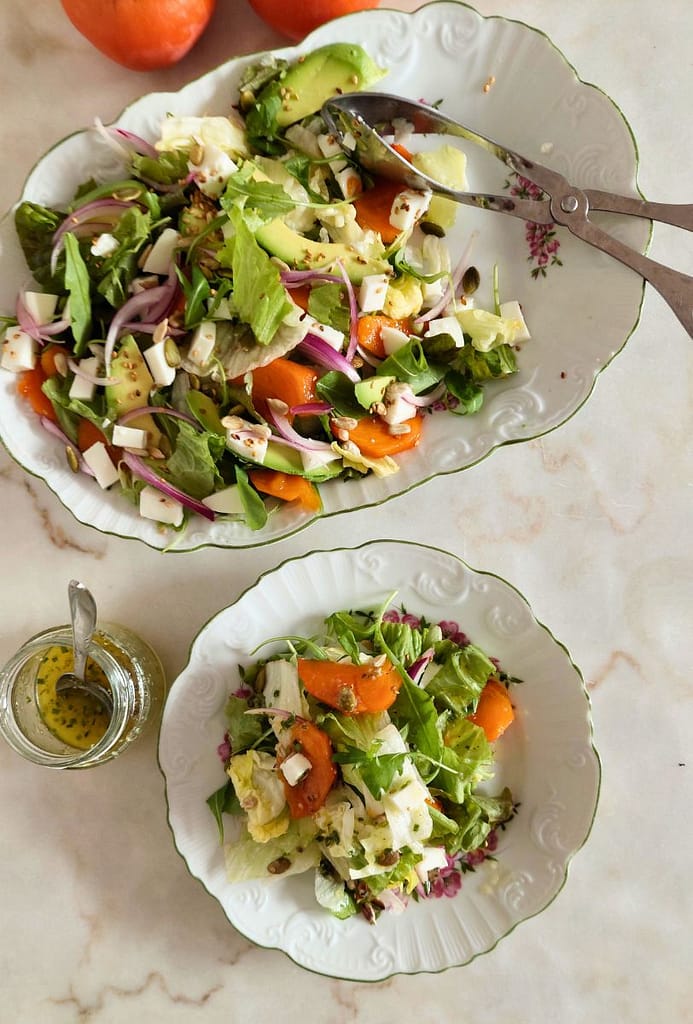 Salada colorida de diospiro tipo maçã com queijo fresco, abacate e sementes servida num prato