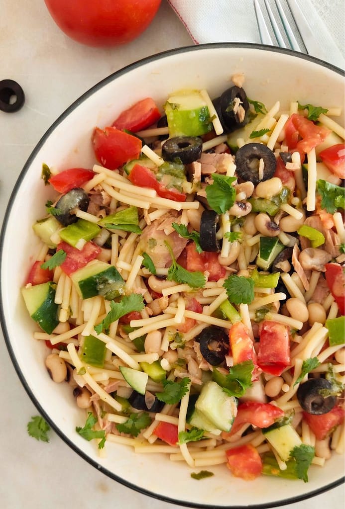 Salada colorida de atum e massa em destaque num prato branco vista de lado, com profundidade e camadas visíveis