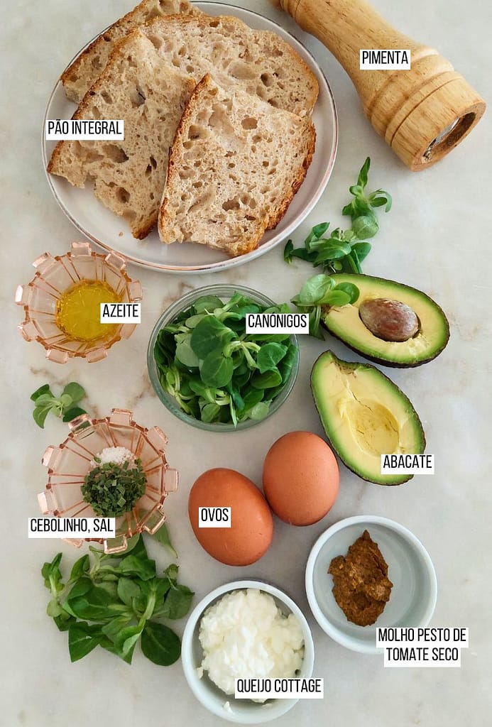 Ingredientes dispostos para pequeno-almoço saudável, azeite, pão, avocado, molho e canónigos