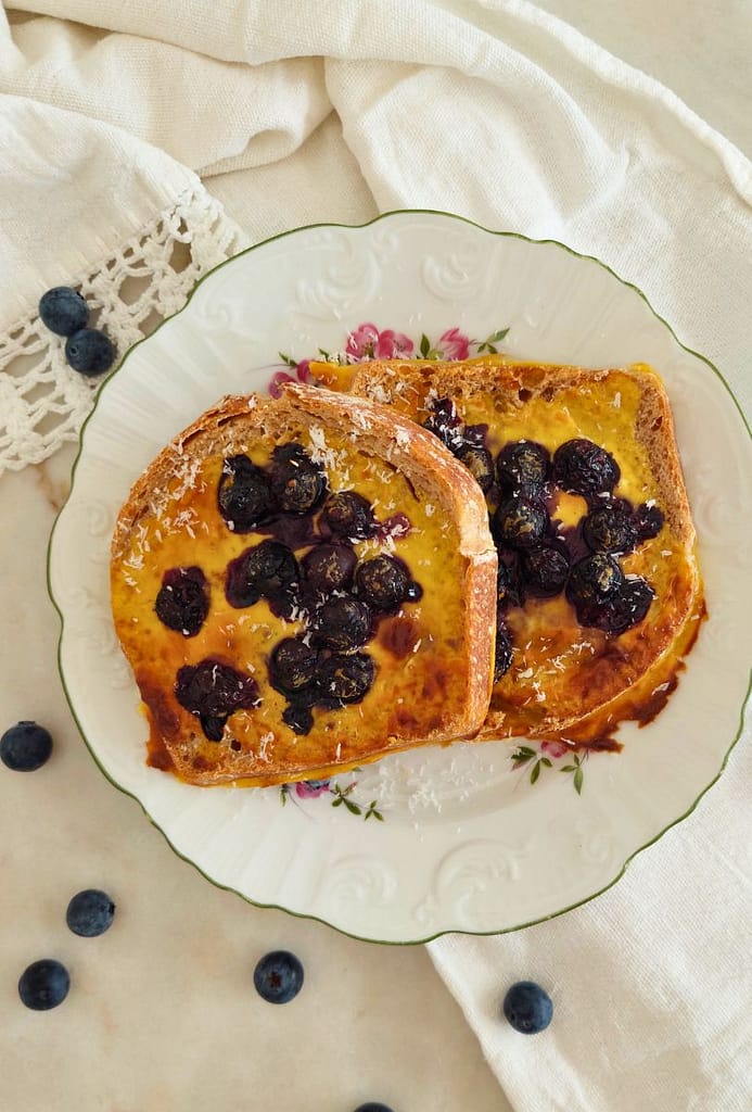 Fatias de pão integral recheadas com creme de iogurte e mirtilos, decoradas com coco ralado, servidas em prato branco
