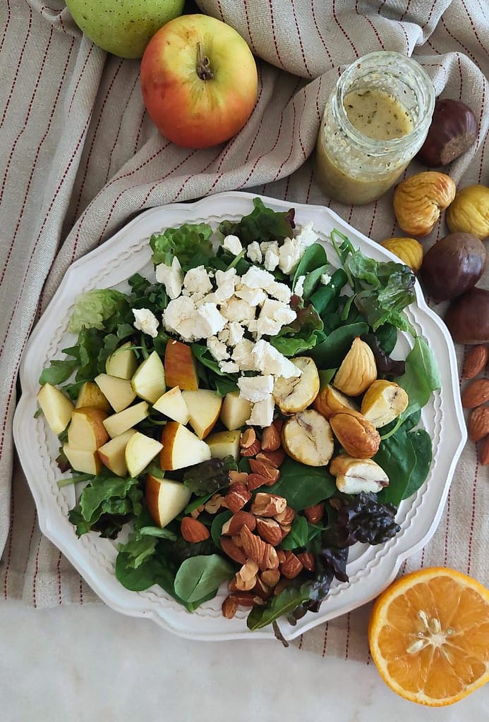 Salada de folhas verdes, Feta, Maçã e Castanhas Assadas temperada com vinagrete caseironum prato branco